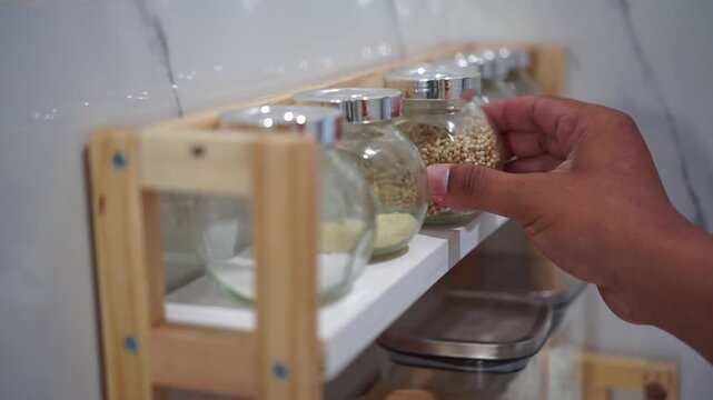 hand placing papper seasoning jar on kitchen rack, organized glass containers, food storage concept.