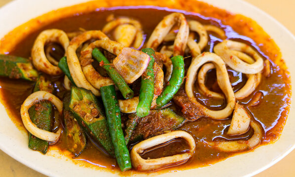 Closeup view of stir-fried squid sotong rings cooked in a rich spicy sambal chili sauce with vegetables on a plate.