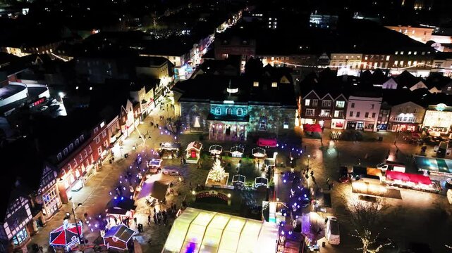 Aerial drone footage at night of Salisbury Guildhall with a festive light projection a decorated Christmas tree and market stalls filling the square