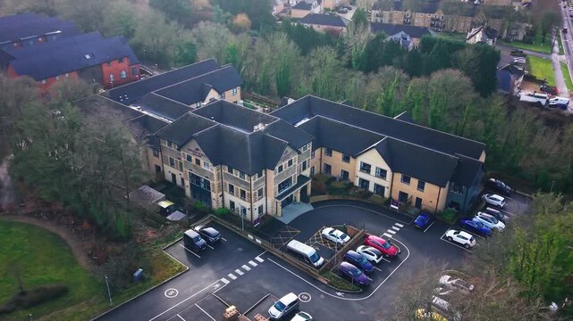 Aerial drone footage of Wilton care home a large stone and gabled building with a car park and surrounding trees in winter