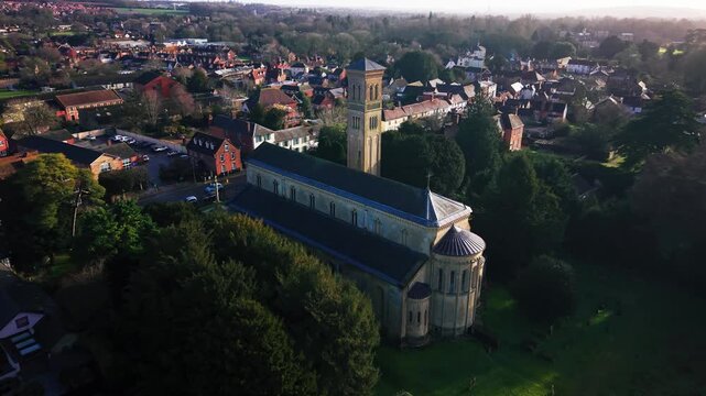 Aerial drone footage of a large stone parish church with a tall Italianate bell tower surrounded by village rooftops and trees