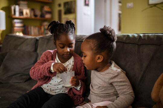 Two young children sharing a snack on living room sofa