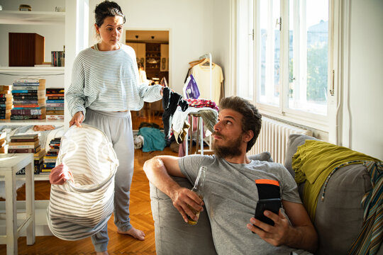 Frustrated woman confronting partner over laundry in messy living room