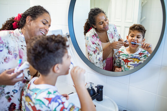 Mother teaching son to brush teeth in home bathroom