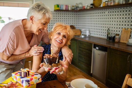 Two senior women celebrating birthday with cake at home kitchen