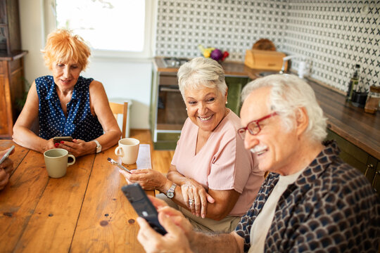Happy seniors using smartphones together at kitchen table