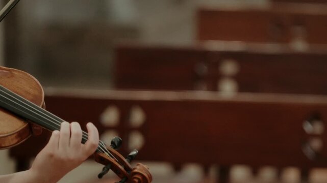 Close up of a hand pressing violin strings on the fingerboard with wooden pews behind