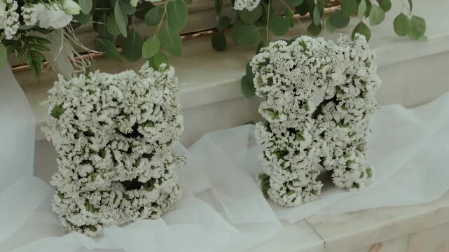 Two white statice flower arrangements resting on marble steps with tulle and eucalyptus