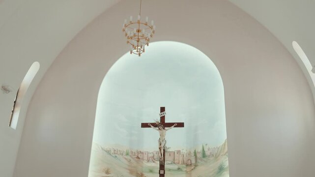Crucifix on a painted Jerusalem mural under a chandelier inside an arched church apse