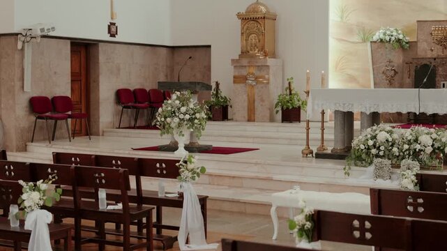 White flower arrangements candlesticks and draped pews decorating a church altar before a wedding