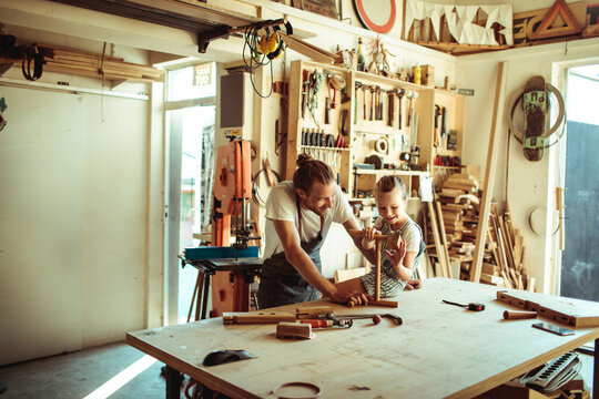 Adult teaching child woodworking in home workshop
