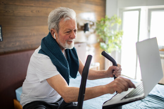 Senior man exercising on stationary bike at home with laptop