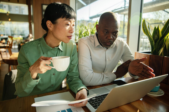 Coworkers reviewing financial report on laptop at cafe