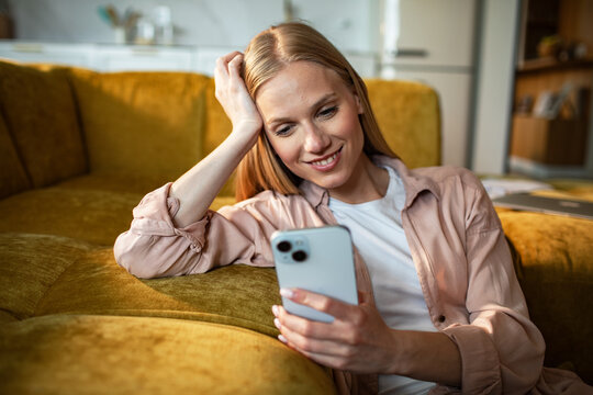 Smiling young woman using smartphone at home on sofa