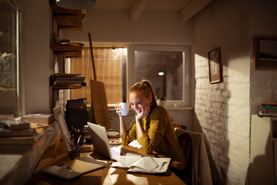 Smiling woman working late at home office with laptop and coffee