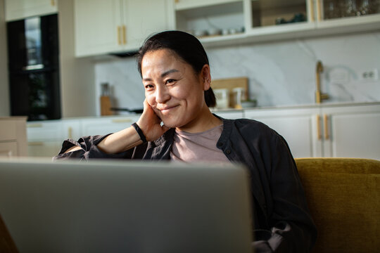 Smiling woman using laptop at home kitchen