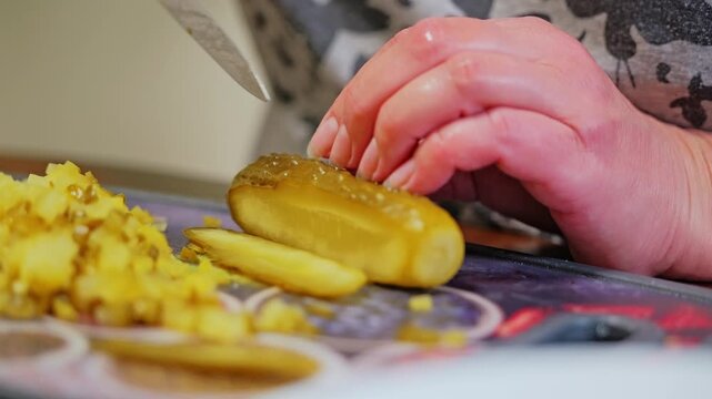 Close-up captures hands slicing pickled cucumber into pieces during kitchen prep