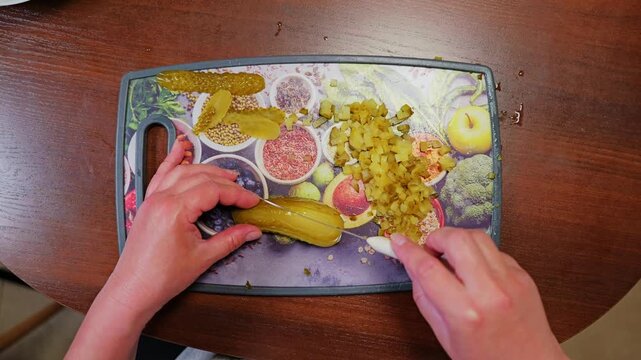 Top-down view captures woman slicing a pickled cucumber in half during food prep