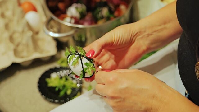 Slow motion captures hands securing herbs onto egg before traditional dyeing