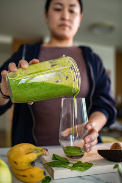 Woman pouring green smoothie in home kitchen