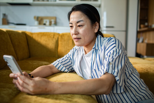 Woman using smartphone on yellow sofa at home