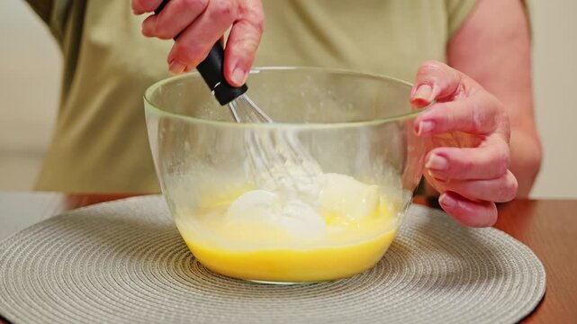 Older woman whisks cottage cheese into batter while preparing homemade curd cake