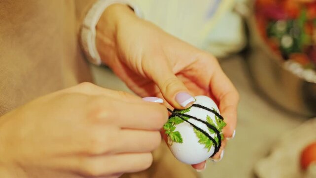 Slow motion, hands tying green herbs onto egg to create botanical patterns