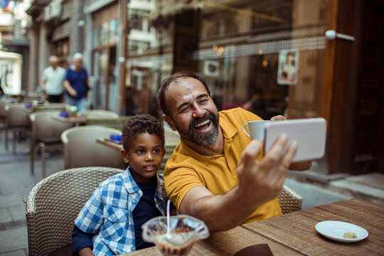 Smiling father and son taking selfie at street cafe