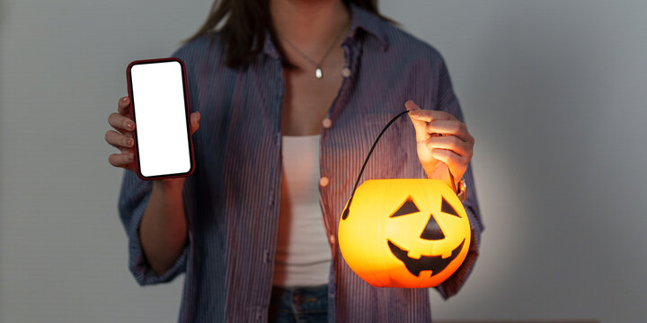 Faceless woman holding smartphone mockup and Halloween pumpkin lantern