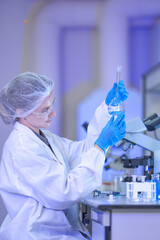 A female science professional in a white coat, protective eyewear and a sterile hairnet holding the...