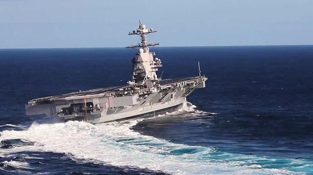 Aircraft carrier maneuvers through deep ocean waters during high-speed naval operations, leaving a dramatic white wake behind.