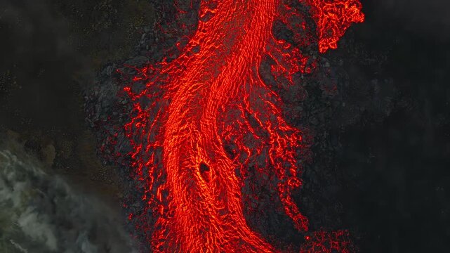 Molten lava flow river moving across dark volcanic landscape