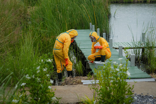 Hazmat suit protective gear respirator scientist environmental testing water sample wetland boardwalk team collects marsh water near dock, cautious fieldwork during contamination investigation
