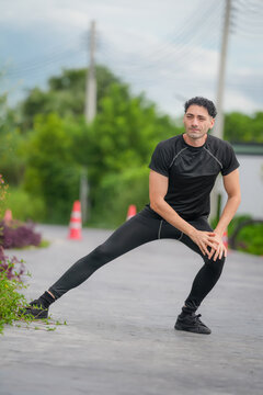 Male athlete stretching lunge warmup outdoor road fitness before workout, adult runner in black sportswear training on pavement, focused expression, copy space