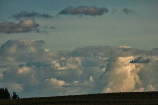 Dramatic clouds gather over a dark, rolling landscape at dusk