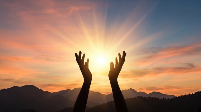 Silhouette of two human hands reaching up towards the bright shining sun setting behind mountain range, beautiful colorful orange and blue sky with clouds, spiritual freedom