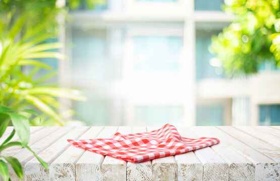 Selective focus.Wooden table with a red and white checkered tablecloth, set against a blurred background of a green outdoor garden and residential area.
