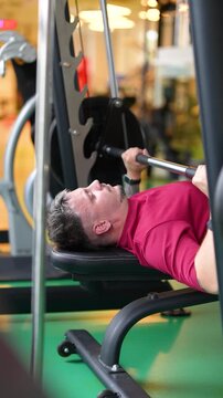 Determined focused athlete lying on bench doing chest press workout in smith machine with barbell, confident man lifting weights in fitness center at training, building physical health and endurance.