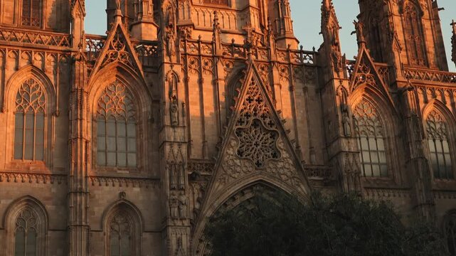 Gothic cathedral spires in Barcelona glow in warm golden sunlight against a clear evening sky, establishing tilt down