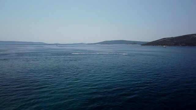 Adriatic Sea near Seget Vranjica, Trogir, Croatia with distant islands and boats, aerial tracking follows speedboat or jetski bouncing across water surface