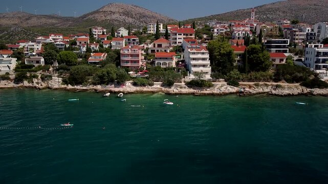 Seget Vranjica, Trogir, Croatia red roof homes border clear Adriatic coast, aerial medium descend approach