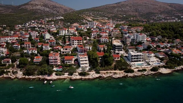 Seget Vranjica, Trogir, Croatia coastal town spreads over Adriatic hillside, aerial descend pan left establishing drone backdrop