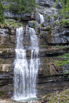 Close-up of a tiered waterfall tumbling down stratified rock into a clear pool. Fresh alpine scene with dynamic water and rugged stone.