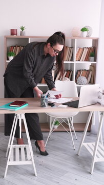Vertical video. Manager paperwork. Office career. Female boss analyzing business document using laptop at desk at professional workplace.