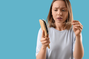 Hair loss and thinning hair problem, young woman looking at hair on brush with worried expression,...