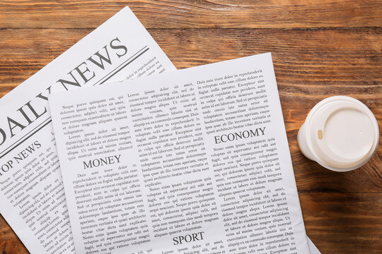 Global news and economic updates daily newspaper with money and sport sections coffee cup on wooden table top view