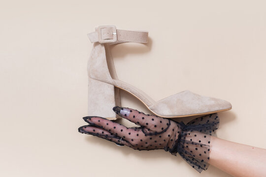 Hand holding a beige high heel shoe with a strap against a light background