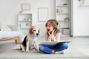 Fototapeta premium Surprised little girl with Beagle dog and book on floor in living room