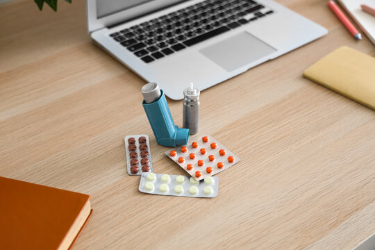 Modern inhaler, asthma aerosol canister and pills on workspace desk, closeup