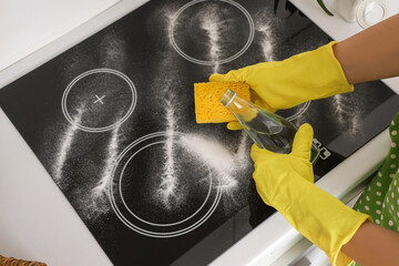 Naklejka premium Housewife cleaning electric stove with vinegar and baking soda in kitchen, closeup